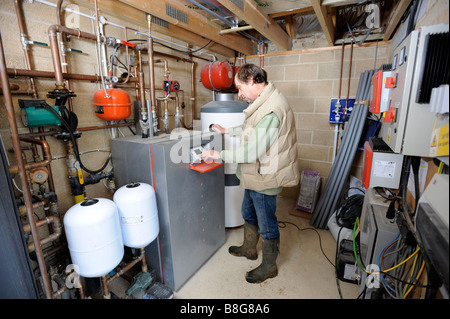 Il proprietario di un'energia efficiente casa regola il pannello di controllo nella camera di pompa di una fonte di massa sistema calore ENERGIA EOLICA INVE Foto Stock