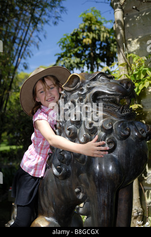 Bambino (6 anni) giocando su uno dei due leoni di bronzo, noto come tempio cani, in Royal Botanic Gardens. Sydney, Australia Foto Stock