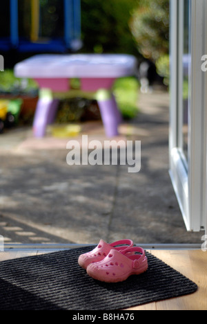 Childs rosa croc stile di gioco all'aperto scarpe seduta sul tappetino della porta mediante una porta aperta. Foto Stock