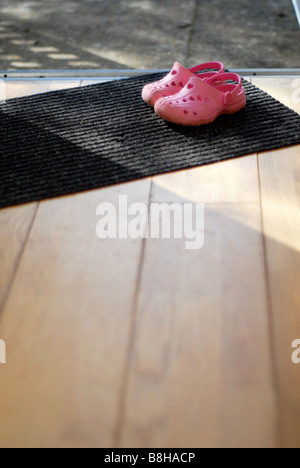 Childs rosa croc stile di gioco all'aperto scarpe seduta sul tappetino della porta mediante una porta aperta. Foto Stock