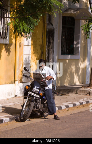 India Pondicherry Rue Dumas uomo seduto sulla moto di lettura quotidiano tamil nel sole al mattino Foto Stock