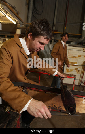 Un professionista soffiatore di vetro richiede un po' di vetro fuso in uscita da un forno pronto a soffiare e la forma in un vaso di vetro o di ornamento Foto Stock