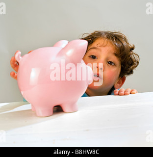 Ragazzo giovane raggiungendo un salvadanaio Foto Stock