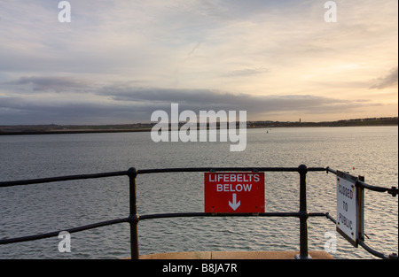 Lifebelt segno che sembra sia rivolta in mare attaccato alle ringhiere in ghisa sul molo di Tynemouth al crepuscolo Foto Stock