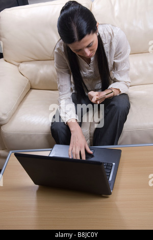 La donna si sedette sul divano facendo shopping online con un computer portatile e una carta di credito Foto Stock