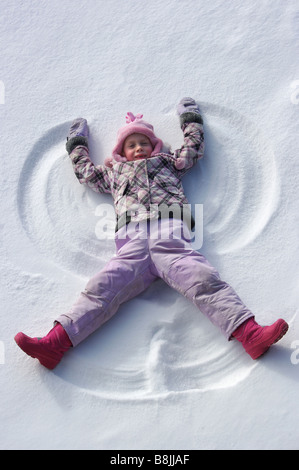 Con polvere di nevicare sul terreno, una bambina giocare intorno rende il primo angelo di neve dell'anno. Foto Stock