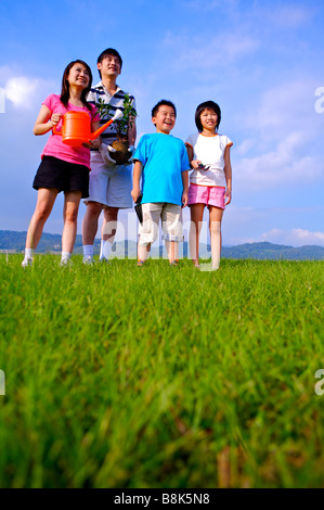 Giovane famiglia con due bambini in piedi sul prato che guarda lontano e sorridente Foto Stock