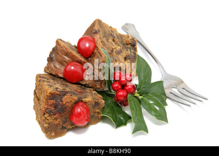 Una deliziosa torta di frutta umido fette guarnendo con ciliegie e holly e isolato su bianco con una forcella Foto Stock