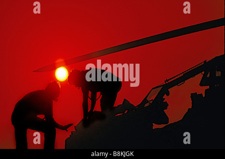 Silhouette con Sun di due tecnici aerospaziali lavorando sul naso dell'elicottero. Foto Stock