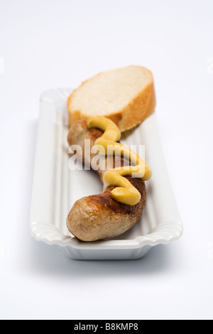 Il tedesco Thüringer Bratwurst con senape e la fetta di pane sul piatto di portata, posto su uno sfondo bianco, vista frontale Foto Stock