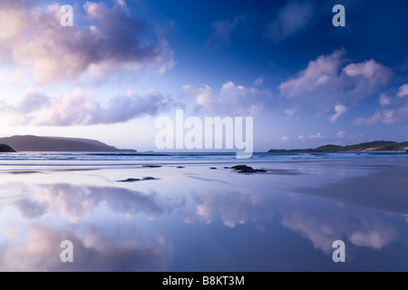 Colorato di blu e viola tramonto a poco profonda spiaggia scozzese, colline in background, le nuvole nel cielo riflettendo sulla spiaggia Foto Stock