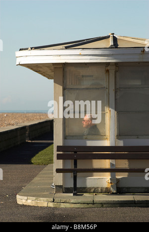 Godendo di mattina inverno Sun in un rifugio a Worthing seafront in West Sussex. Foto Stock