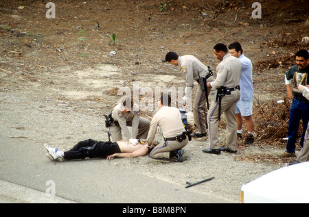 California Highway Patrol officers adminsister CPR ammanettato prigioniero sul lato dell'autostrada. Foto Stock