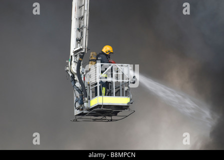 Vigile del fuoco nella piattaforma idraulica gabbia Indossare respiratore combattimenti grande fabbrica di fuoco Foto Stock