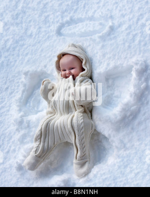 Una bambina fa un angelo di neve pattern nella neve. Foto Stock