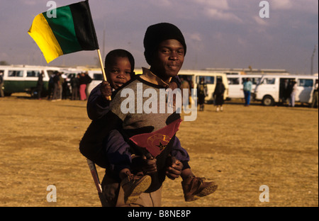 Un uomo porta un bambino sulla schiena sventolare la bandiera dell'ANC a Soweto lancio di S.A.C.P (Sud Africano partito comunista) Foto Stock