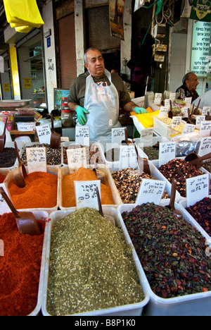 Negoziante affacciato su contenitori di esotica essiccato medio spezie orientali a Shuk Ha Carmelo mercato aperto Foto Stock