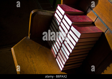 Inno libri meticolosamente impilati su un di legno pew in una piccola chiesa di campagna. Foto Stock