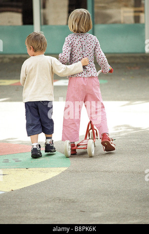 I fratelli in cammino insieme, ragazza spingendo scooter, ragazzo del braccio attorno alla ragazza in vita, vista posteriore Foto Stock