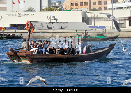 Trasporto nel Dubai Creek vicino al taxi acquatico Abras e la folla di passeggeri include gabbiani e biblioteca pubblica sul lungofiume oltre gli emirati arabi uniti Foto Stock