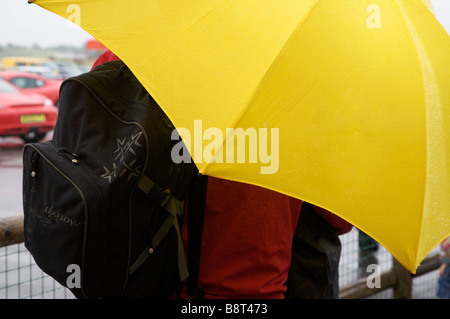 Spettatore rifugiandosi sotto Ombrello giallo sul giorno di pioggia a Thruxton Motor Racing, circuito di Thruxton, Hampshire, Regno Unito Foto Stock