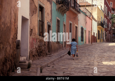 Donna che cammina giù per una strada ricca di stile coloniale spagnolo delle case nella città di Guanajuato, Messico Foto Stock