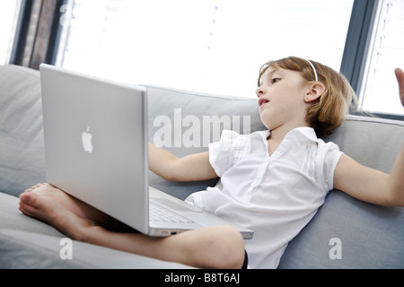 La ragazza si siede su un divano con un notebook Foto Stock