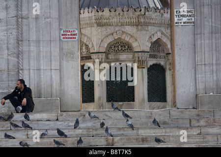 L'uomo circondato da piccioni in attesa all'ingresso della nuova moschea di Istanbul. Foto Stock