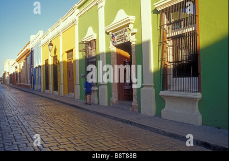 Donna che cammina giù per una strada fiancheggiata con coloniale spagnola ristrutturata case nella città di Campeche, Messico Foto Stock