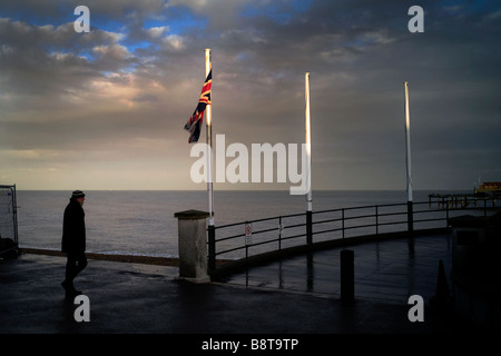 Un uomo di fare una passeggiata lungo la parte anteriore di un inglese località balneare nel primo inverno Foto Stock