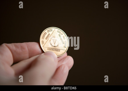 Mano che tiene un Alcolisti Anonimi, monete o 'chip' celebrazione numero di anni sobrio Foto Stock