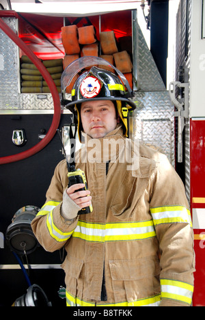 Firefighter maschio radio di contenimento nella parte anteriore del camion dei pompieri indossando ingranaggio bunker e casco Foto Stock