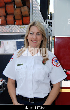 Donna sorridente pompiere paramedico in uniforme del vestito in posa nella parte anteriore del motore Fire Foto Stock