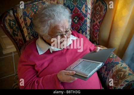 L' e-book di lettura della signora anziana 80-90 a casa da sola isolando covid-19 gode dell'uso della nuova tecnologia digitale con il dispositivo elettronico di lettura del libro eReader Foto Stock