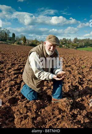 Il contadino di esaminare il terreno nel campo arato Foto Stock