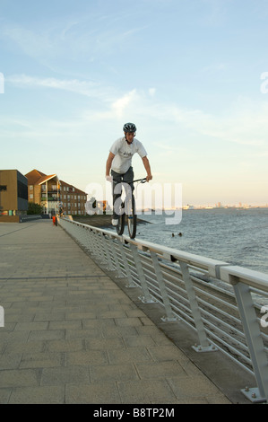 Ragazzo equitazione mountain bike lungo la parte superiore del corrimano sul lungomare dal fiume Humber, East Yorkshire, Regno Unito Foto Stock