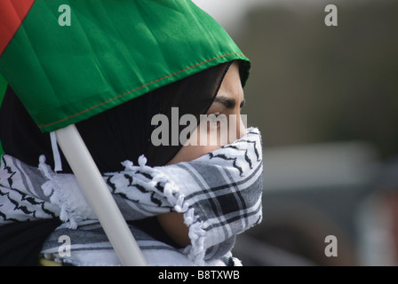 Una giovane donna palestinese copre il suo volto con una tradizionale sciarpa di keffiyeh o kufiya a rete bianca e nera durante una protesta in Cisgiordania Foto Stock