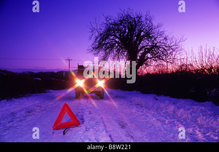 Il veicolo che si muove in basso lungo la neve legato country road dal triangolo di segnalazione al crepuscolo vicino a Leeds Yorkshire Regno Unito Foto Stock