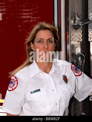 Donna pompiere paramedico in uniforme del vestito in posa nella parte anteriore del motore Fire Foto Stock