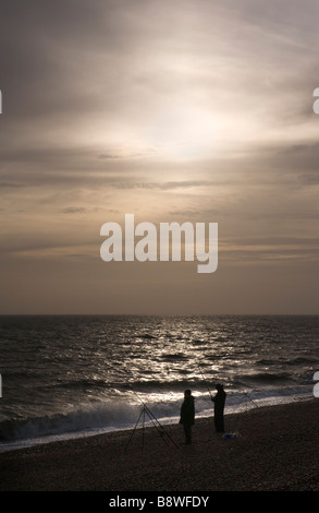 Una silhouette di due pescatori di mare sulla spiaggia a Dengemarsh Beach sulla costa a Dungeness, Kent Foto Stock