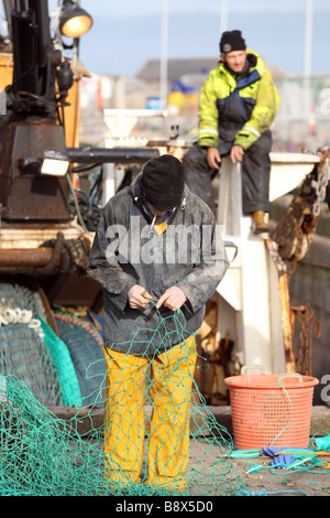 Mare del Nord i pescatori rammendo e riparazione di reti da pesca nel porto a Peterhead, Aberdeenshire, Scotland, Regno Unito Foto Stock