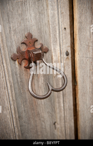 Ferro battuto respingente porta la manopola di impugnatura a forma di cuore su un vecchio weathered porta in legno Foto Stock