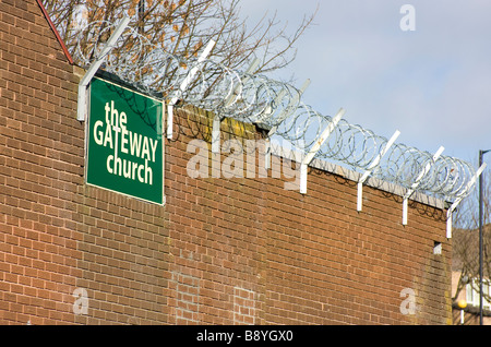 Bobine di filo spinato attaccato al muro di mattoni della chiesa gateway benwell contro il cielo blu con acciaio zincato staffa di supporto Foto Stock