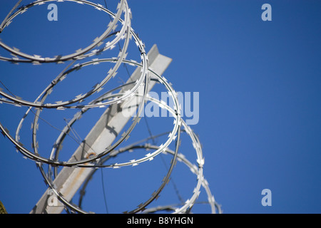 Bobine di filo di rasoio contro il cielo blu con acciaio zincato staffa di supporto Foto Stock