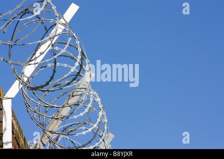 Bobine di filo spinato attaccato al muro di mattoni contro il cielo blu con acciaio zincato staffa di supporto Foto Stock