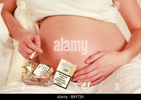 Primo piano di una di Fumare in gravidanza stomaco womans e salute segni di avvertenza sulle sigarette pacchetti fag posacenere pieno nocivi feto Foto Stock