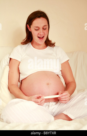 Una giovane donna incinta guarda al risultato di una gravidanza home kit di prova con una lieta sorpresa felice espressione Foto Stock