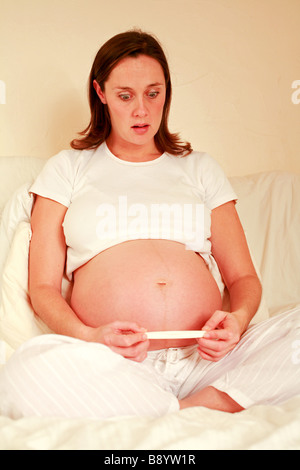 Una giovane donna incinta guarda al risultato di una gravidanza home kit di prova con una sorpresa scioccato startled expression Foto Stock