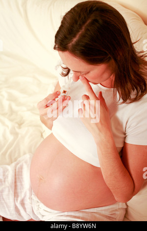 Giovane donna incinta con esposti bump stomaco feto feto si rilassa in casa e odora di colla tossici per ottenere un prodotto chimico ad alta Foto Stock