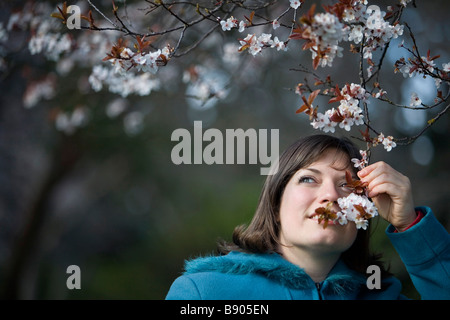 Una giovane donna odori alcuni fiori di ciliegio in Beacon Hill Park, Victoria, British Columbia, Canada. Foto Stock